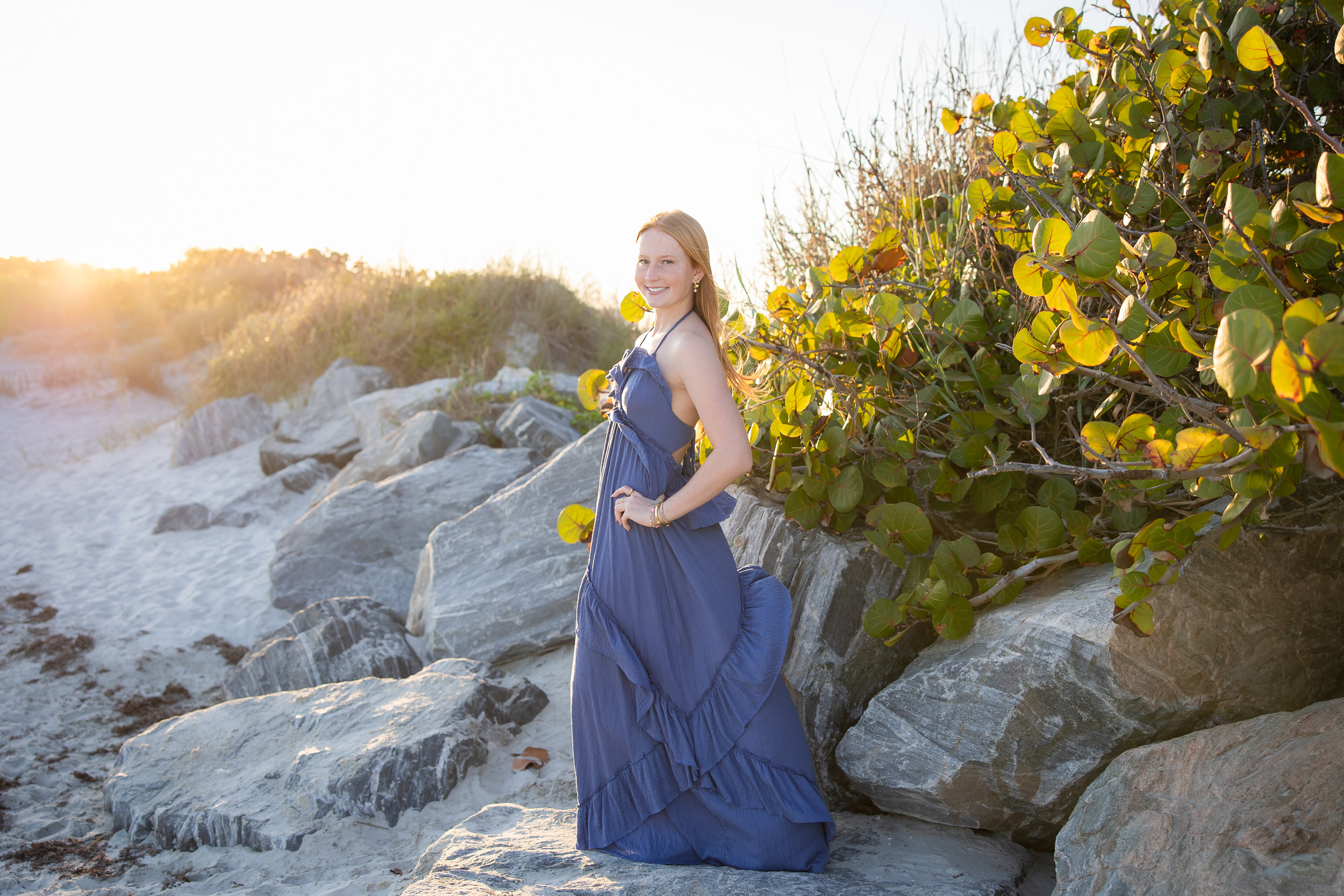 Senior girl wearing a blue dress among the rocks during a Jetty Park senior photography session in Cape Canaveral, Florida.