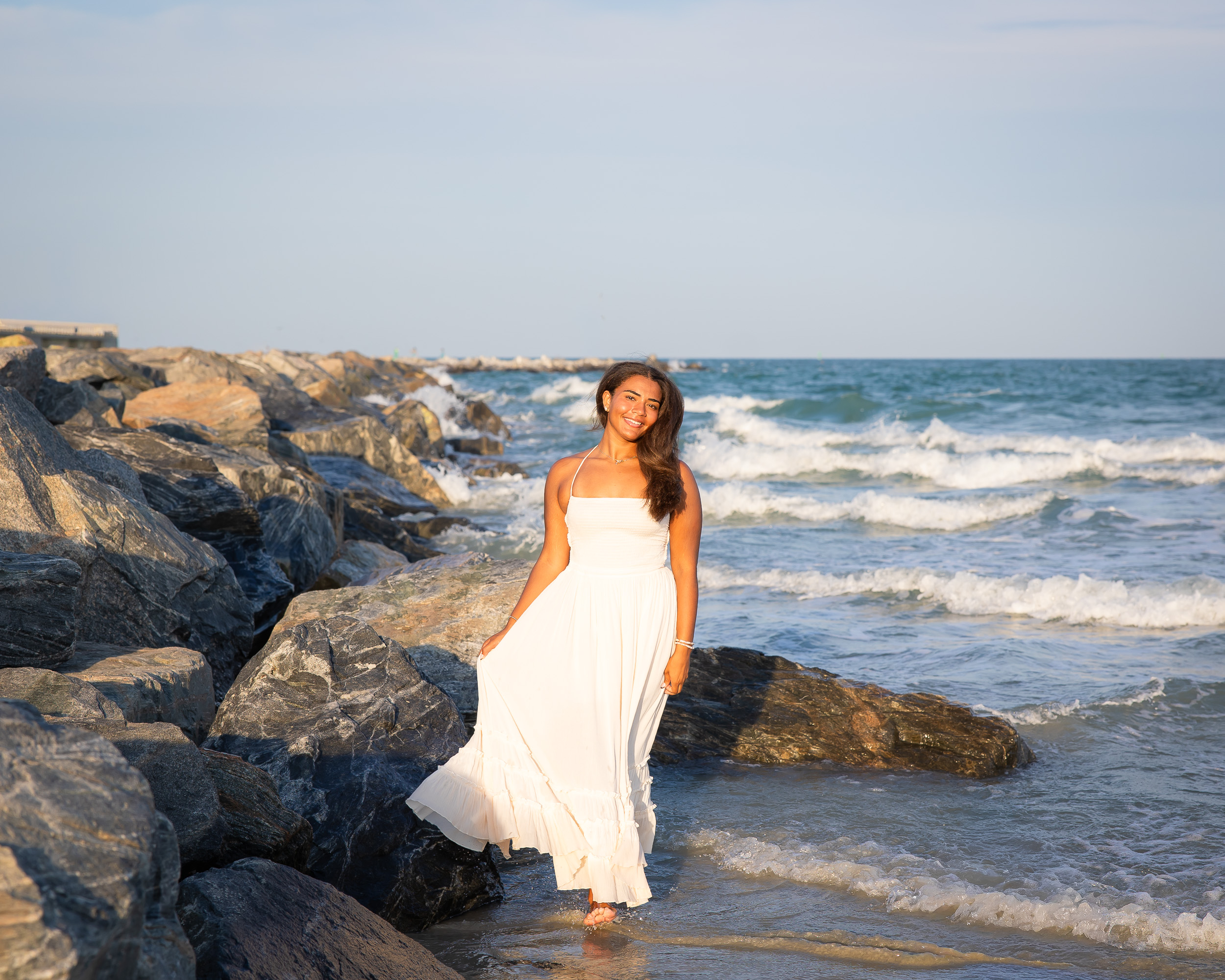 Senior girl in a white dress posing on the rock jetties at Jetty Park in Cape Canaveral, Florida.