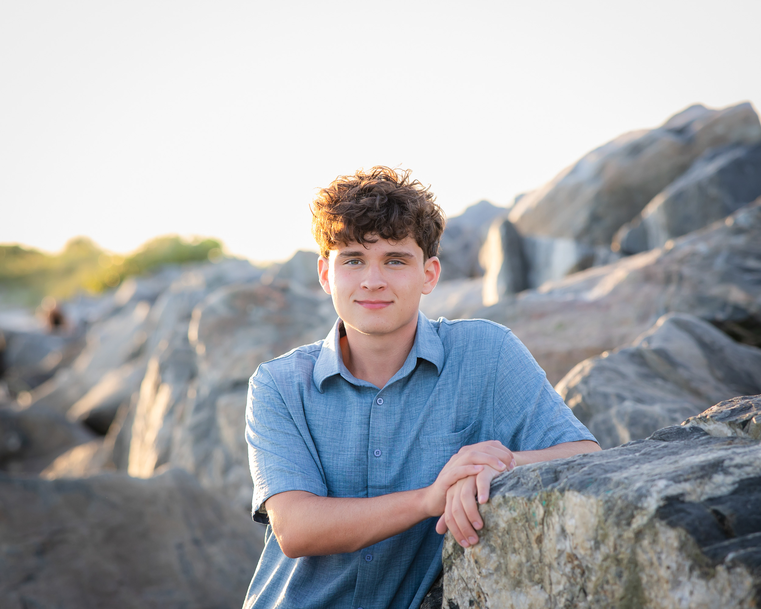 High school senior boy sitting on the rock jetties during a senior photo session at Jetty Park in Cape Canaveral, Florida.