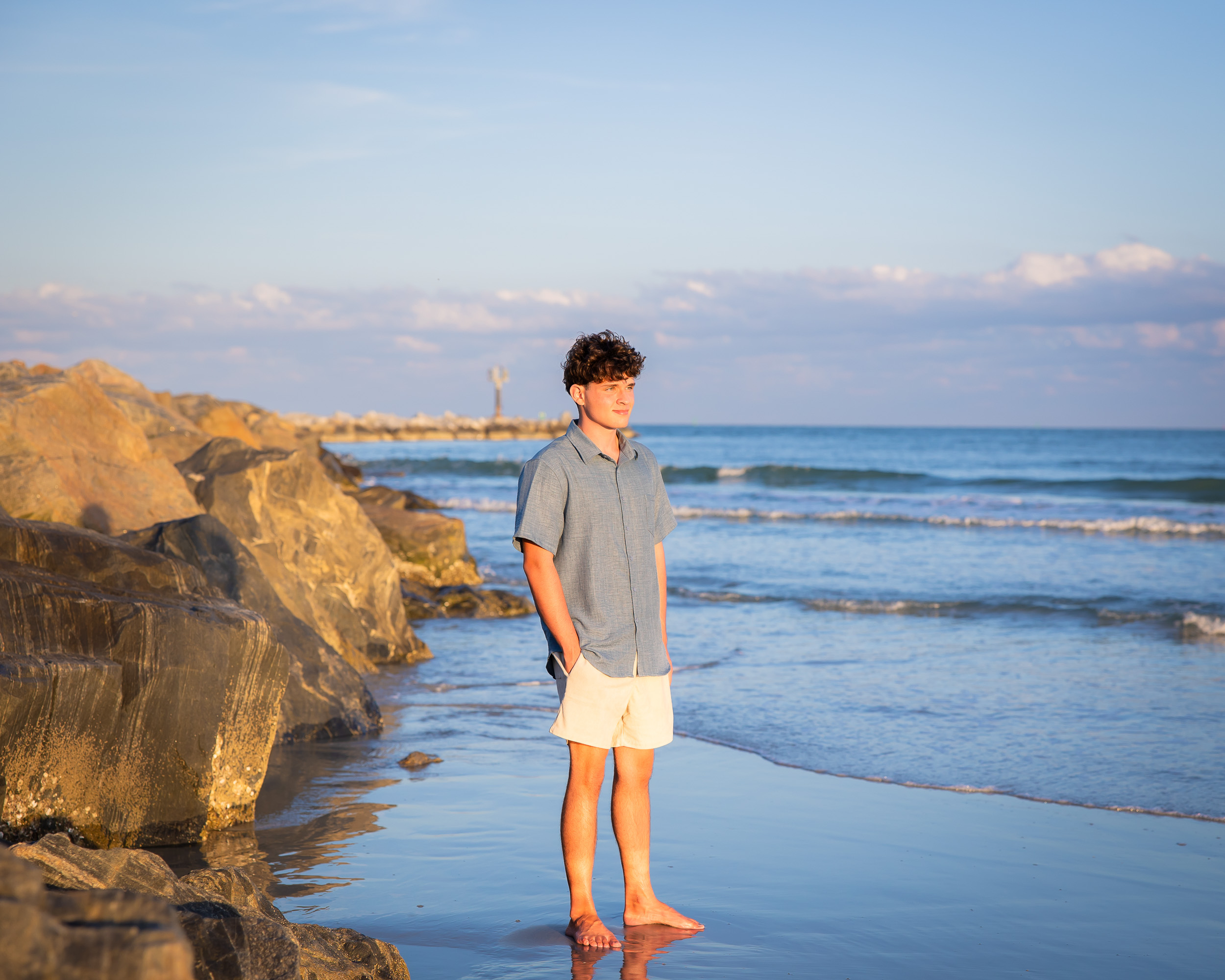 Senior guy standing barefoot on the shoreline during a Jetty Park senior photography session in Cape Canaveral, Florida.