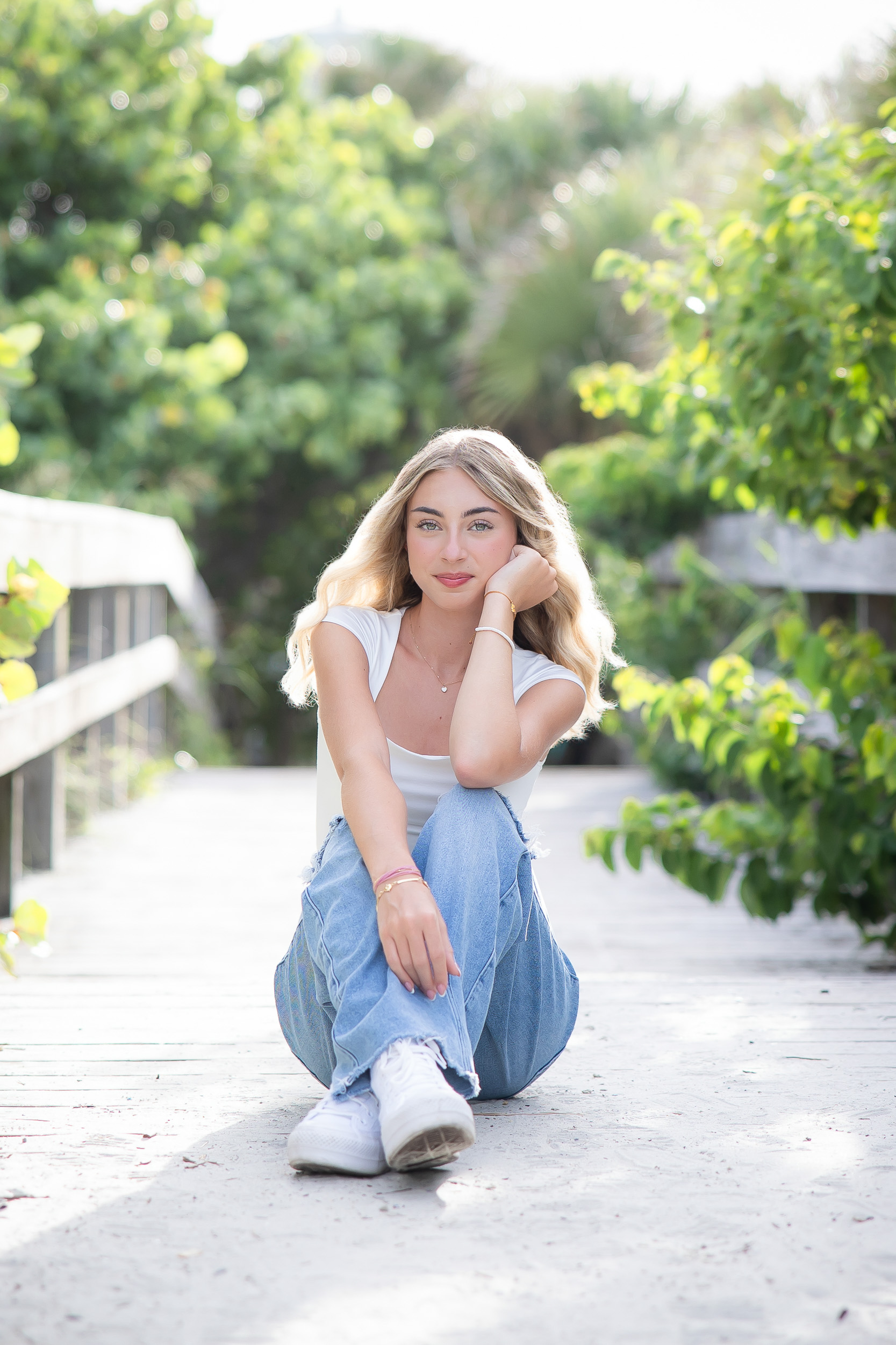 Senior girl sitting on the Jetty Park boardwalk surrounded by greenery.