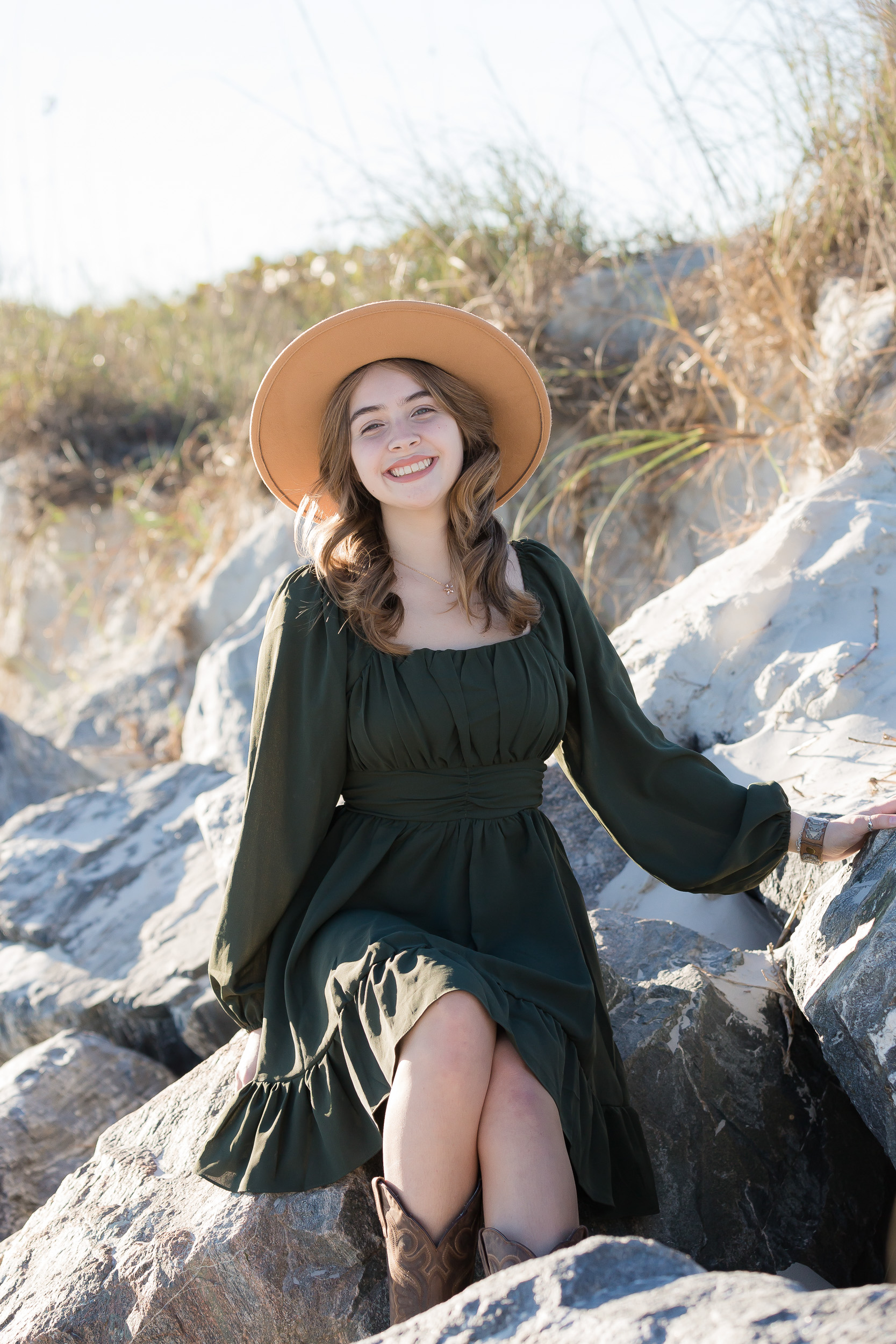 High school senior girl wearing a green dress and wide-brim hat posing in the sea oats at Jetty Park in Cape Canaveral, Florida.