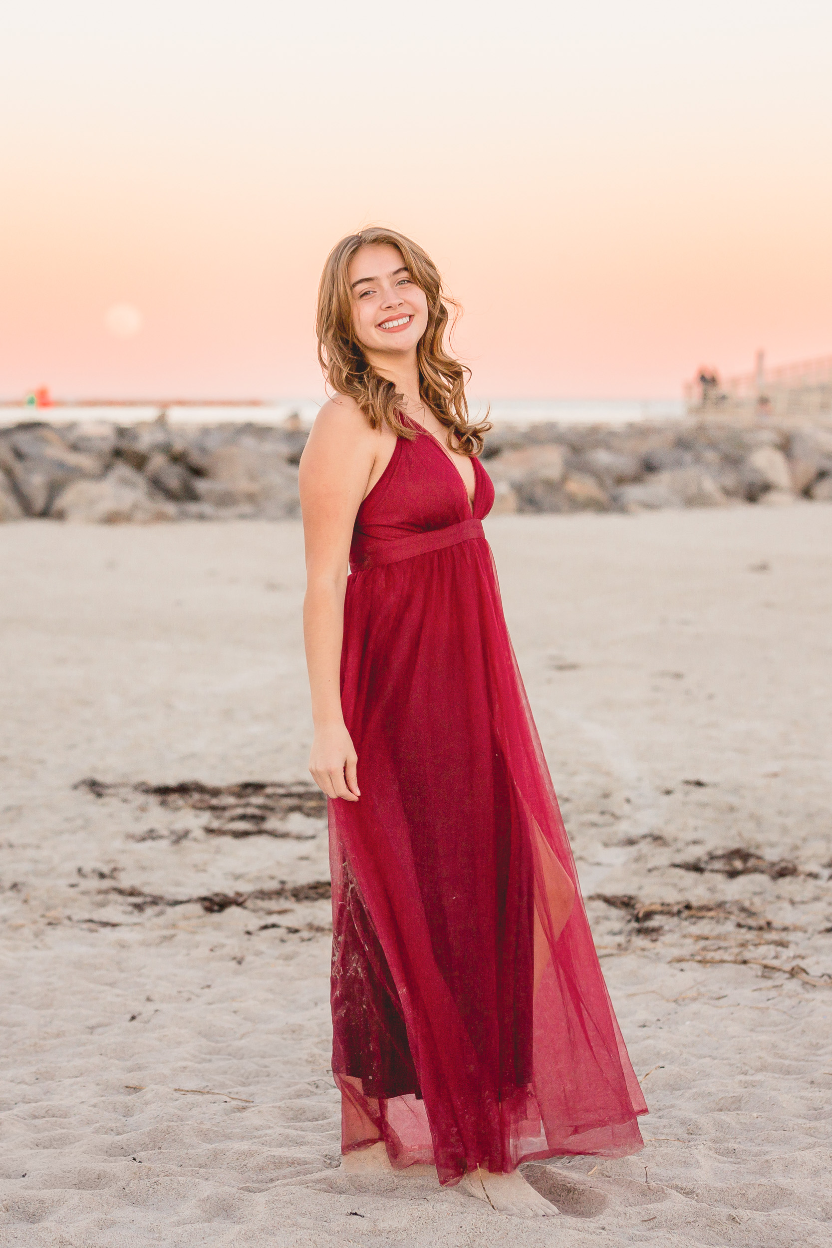 Senior girl in a red dress during sunset at Jetty Park in Cape Canaveral, Florida.