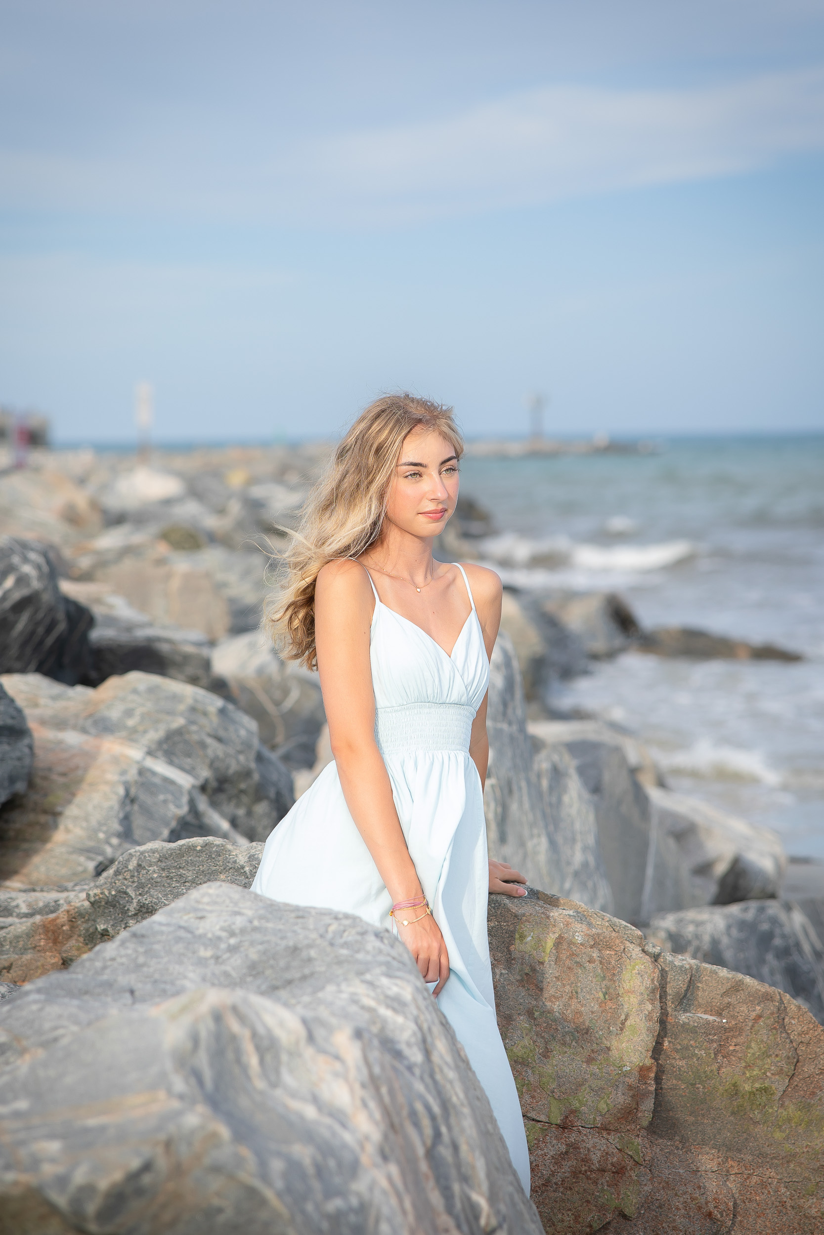 Senior girl in a light blue dress posing on the rocks during a Jetty Park senior photography session in Cape Canaveral, Florida.